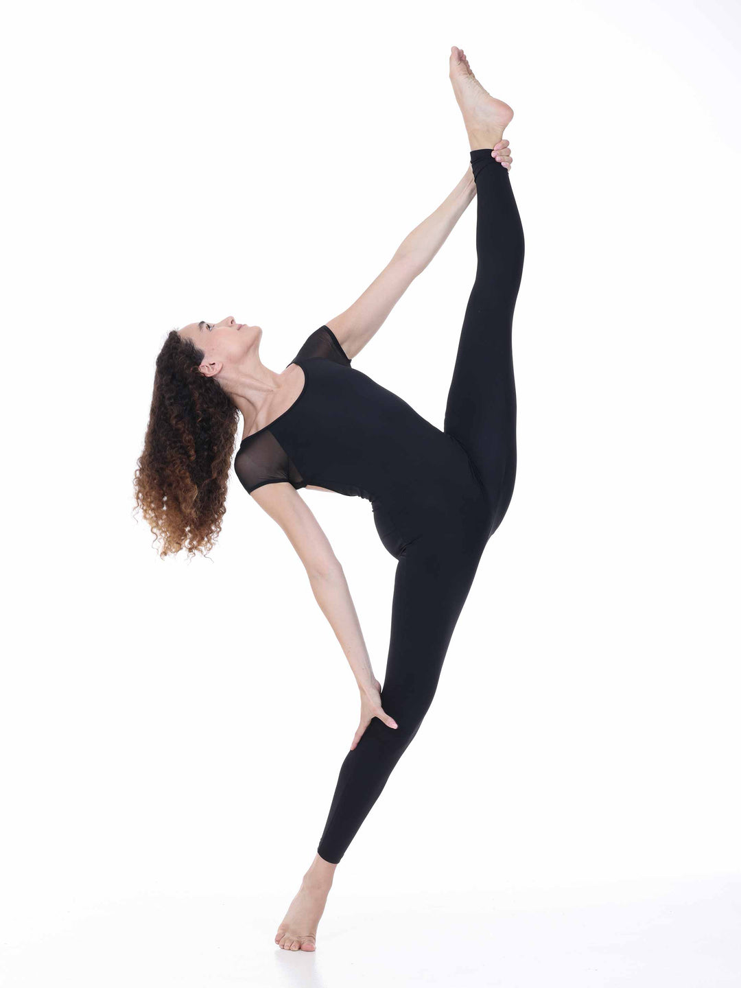 Danseuse portant la combinaison de danse Sway – modèle Sheer Cap Sleeve Dance Unitard en noir, réalisant une extension de jambe haute en position de danse contemporaine, sur fond blanc.