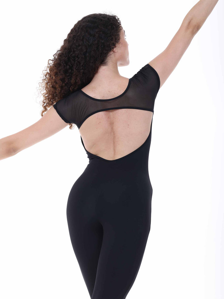 Danseuse portant la combinaison Sway – modèle Sheer Cap Sleeve Dance Unitard en noir, levant gracieusement un bras en pose de danse classique, sur fond blanc.