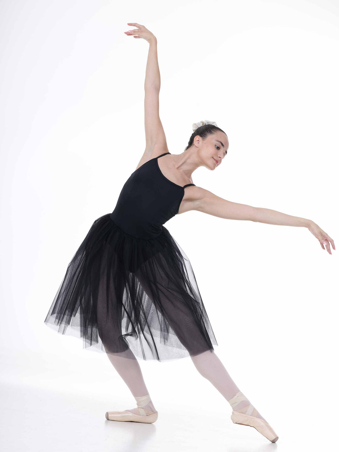 Danseuse en plein mouvement de ballet, robe tutu noire aérienne – bretelles fines et jupe en tulle vaporeuse.