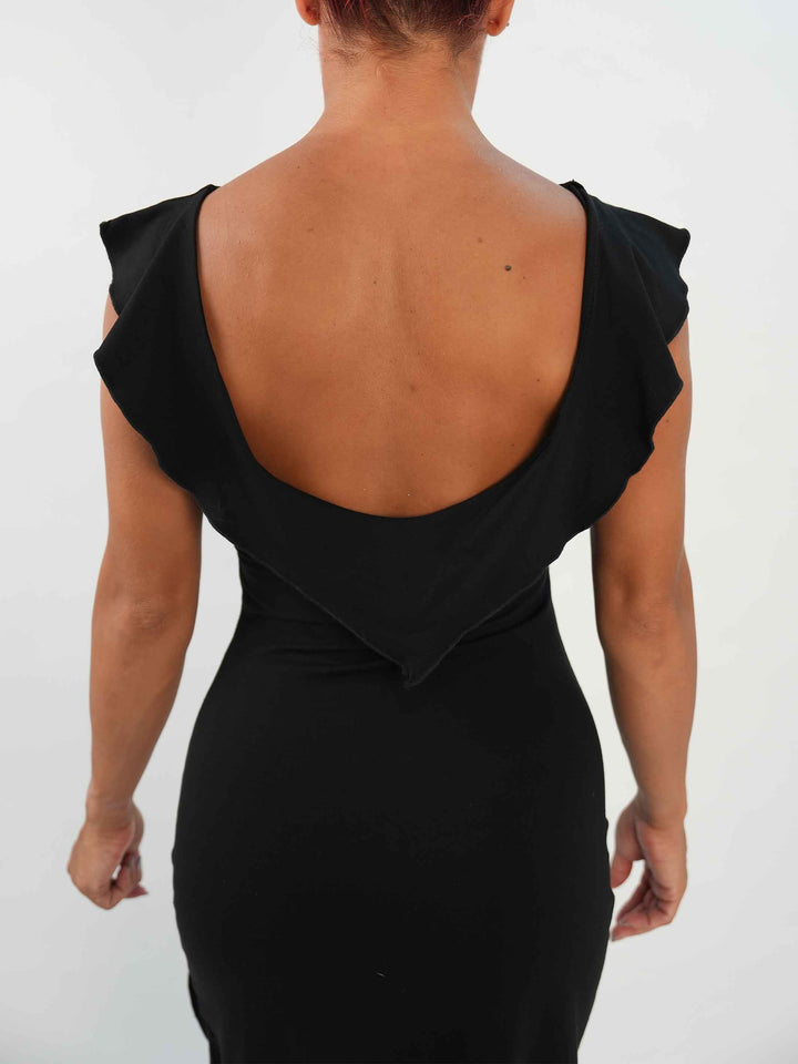 Femme portant une robe noire de danse latine sans manches, avec encolure volantée et ourlet asymétrique, associée à des collants résille et des chaussures de danse ornées. Tenue élégante et fluide, parfaite pour la salsa ou le ballroom. - vue de l'arrière