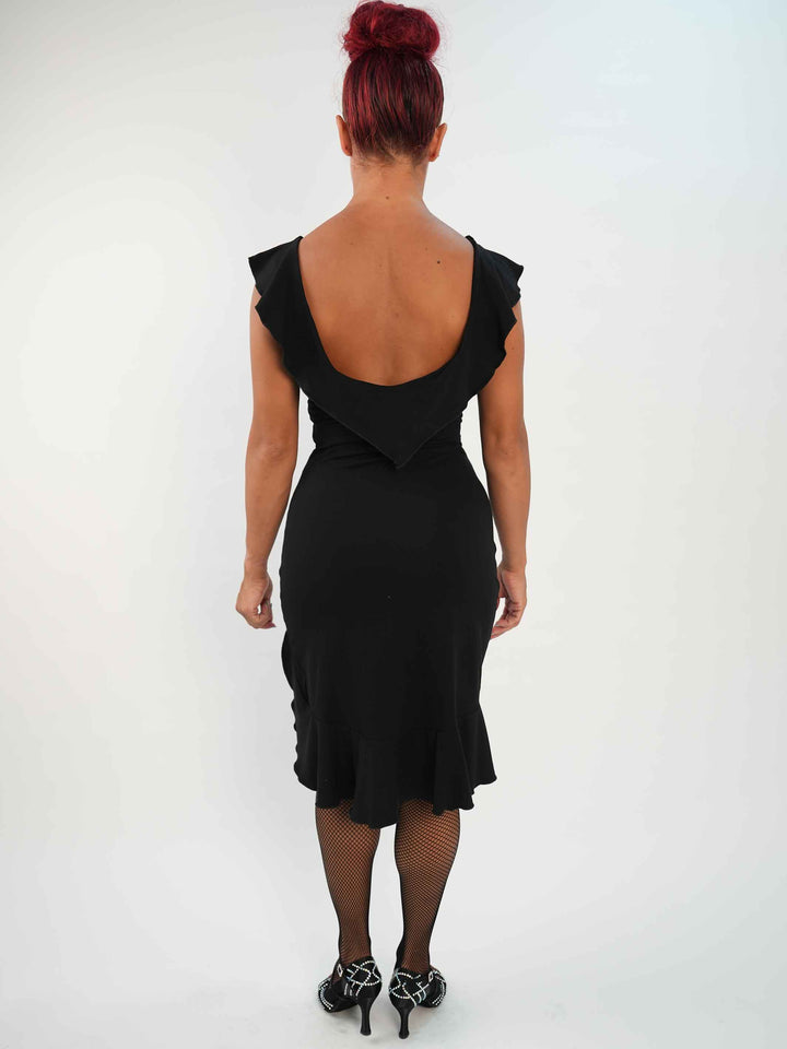 Femme portant une robe noire de danse latine sans manches, avec encolure volantée et ourlet asymétrique, associée à des collants résille et des chaussures de danse ornées. Tenue élégante et fluide, parfaite pour la salsa ou le ballroom. - vue de l'arrière