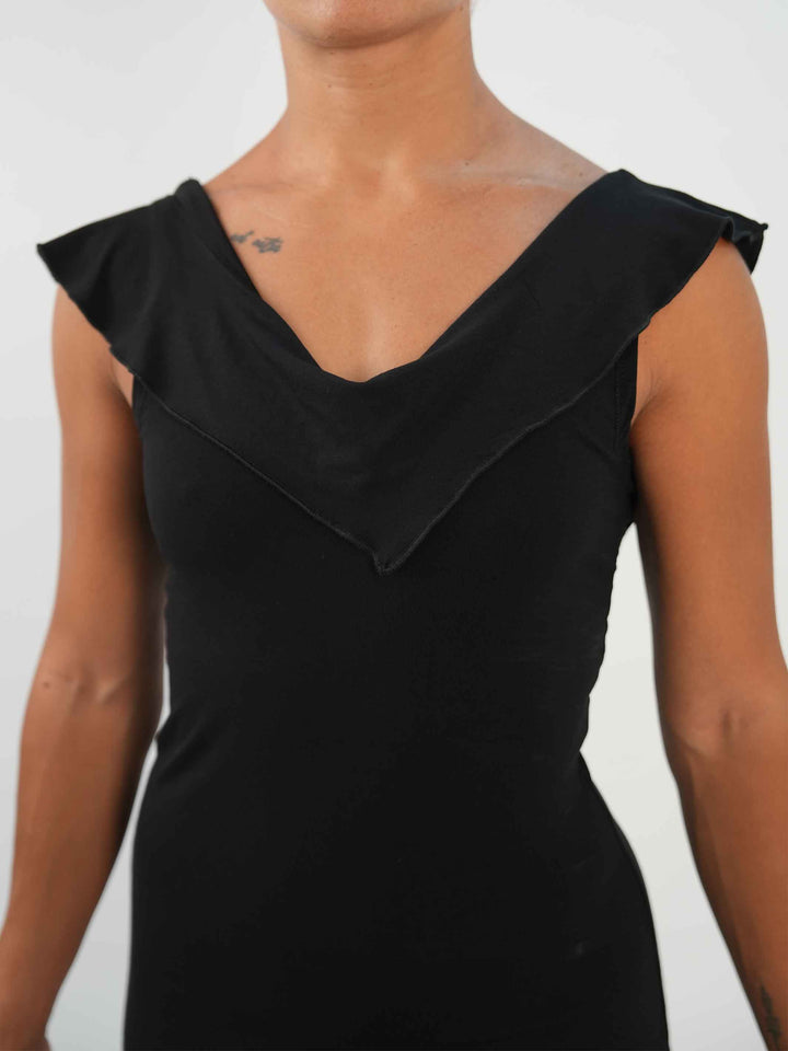 Femme portant une robe noire de danse latine sans manches, avec encolure volantée et ourlet asymétrique, associée à des collants résille et des chaussures de danse ornées. Tenue élégante et fluide, parfaite pour la salsa ou le ballroom. - gros plan de la vue de face