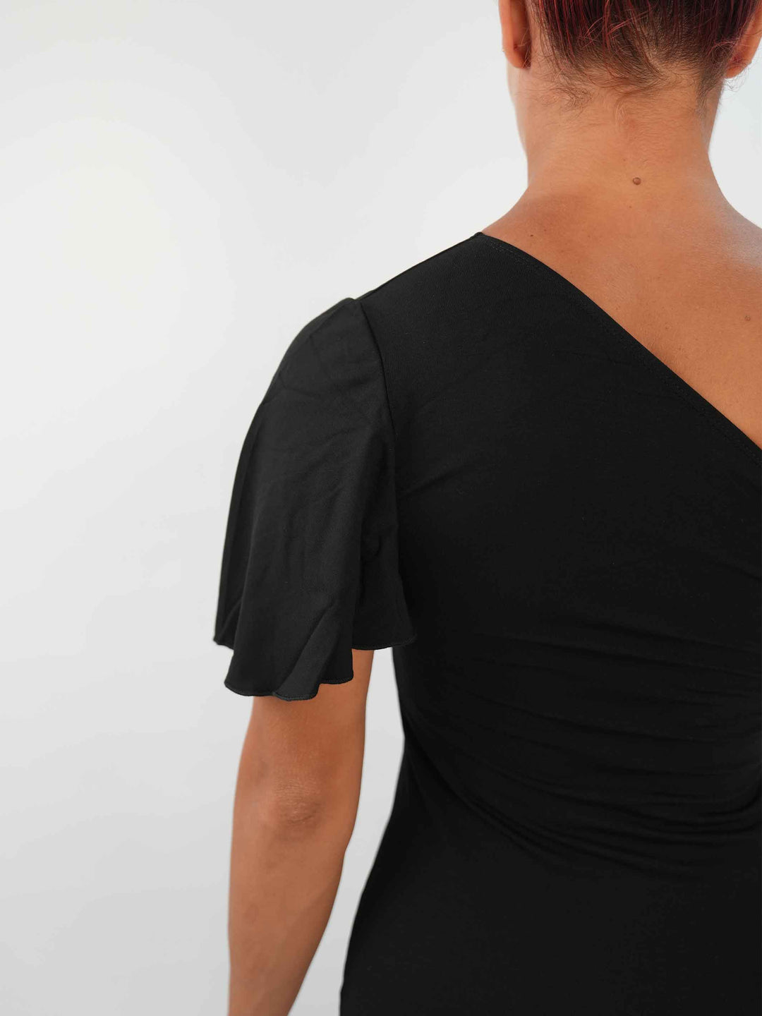 Femme portant une élégante robe latine noire asymétrique avec une manche volante, jupe fluide à godets, idéale pour la salsa, la bachata ou autres danses latines. - gros plan